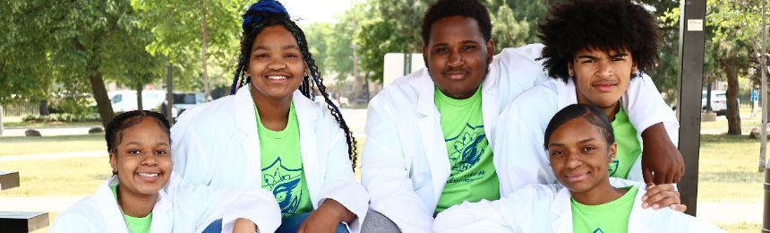 5 students sitting outside wearing white medical coats